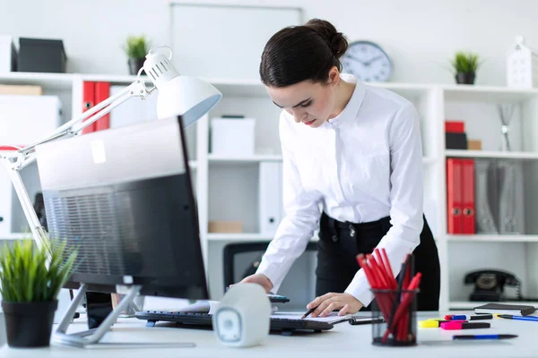 Een jong meisje in het kantoor is permanent in de buurt van de tabel, het bezit van een potlood en een rekenmachine in haar hand en kijkend naar de documenten. — Stockfoto