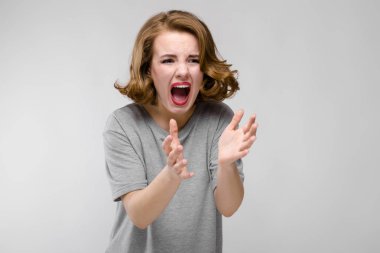 Gri T-shirt gri bir arka plan üzerine sevimli genç kız. Kız çığlıklar