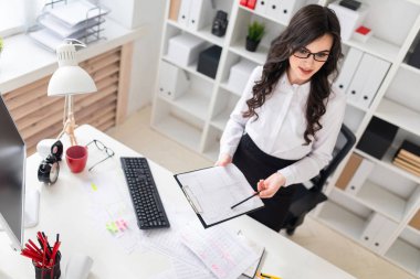 Güzel bir genç kız bir Ofis Masası duruyor ve onun elinde bir levha notları ve bir kalem için tutar.