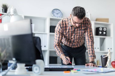 Bir adam ofiste masanın yanında duruyor ve bir işaretleyici manyetik tahtaya çizer.