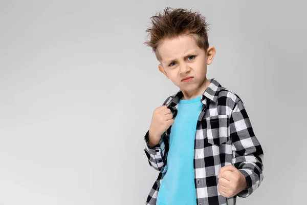 En stilig pojke i en rutig skjorta, ljusblå skjorta och jeans står på en grå bakgrund. Pojken står i ställningen för en boxare — Stockfoto