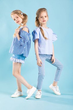 Girls twins in light blue clothes are posing on a blue background. clipart