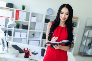 Kırmızı elbiseli güzel genç kız ofiste duran ve bir defter ve bir kalem tutan.