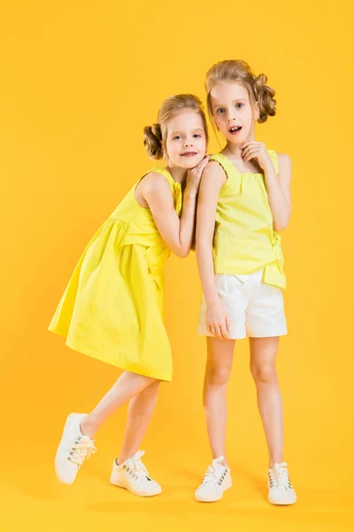 Les filles des jumeaux se tiennent ensemble sur un fond jaune . — Photo