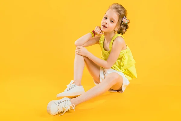 Egy tizenéves lány ül a sárga háttér. — Stock Fotó