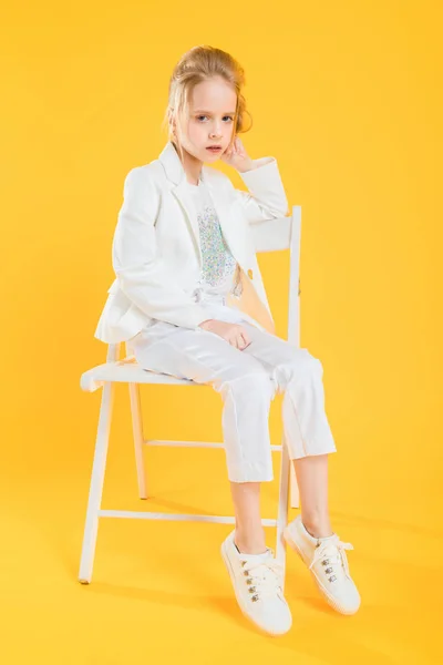 Egy tizenéves lány a fehér ruhákat ül egy széken, egy sárga háttér. — Stock Fotó