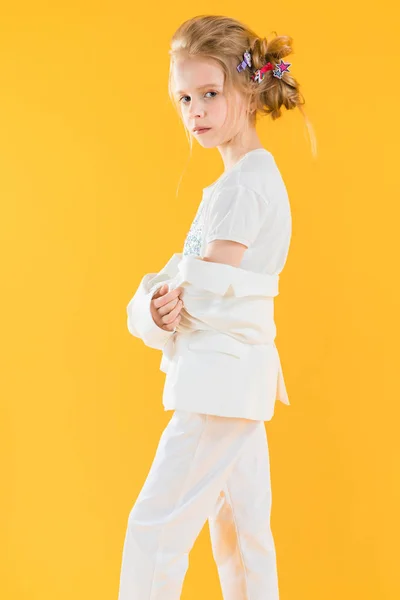 Uma adolescente de roupas brancas posando em um fundo amarelo. A menina baixou o casaco para os cotovelos. — Fotografia de Stock