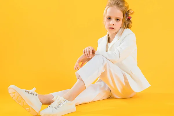 Ein junges Mädchen in weißen Kleidern sitzt und streckt ihre Beine vor einem gelben Hintergrund. — Stockfoto