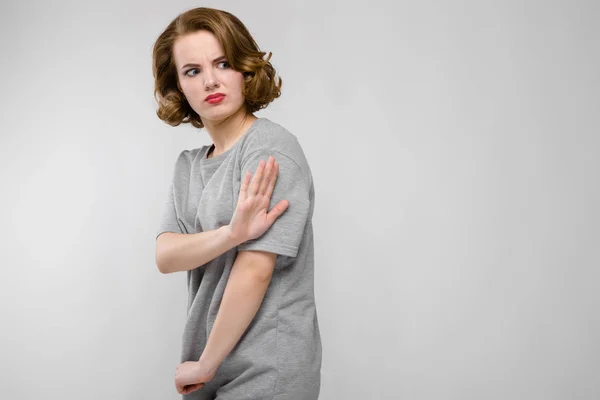Charmante jonge meisje in een grijs T-shirt op een grijze achtergrond. Het meisje vertoont een hand een stop — Stockfoto