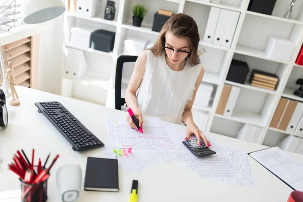 Een jong meisje in het kantoor een roze marker houdt in haar hand en rekent op een rekenmachine. — Stockfoto