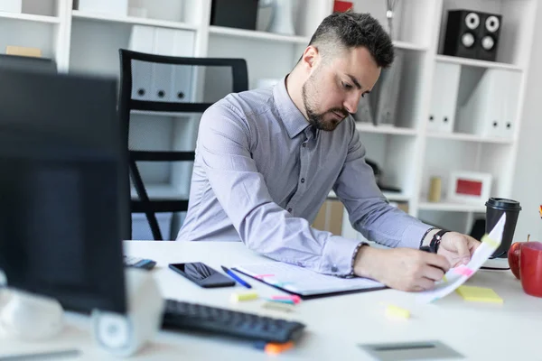 Молодой человек в офисе сидит за столом, держит маркер в руке и работает с документами . — стоковое фото