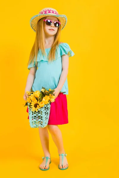 Ragazza con i capelli rossi su sfondo giallo. Una ragazza affascinante in abiti estivi luminosi tiene in mano un cesto di girasoli . — Foto Stock