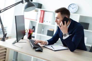 Genç bir adam ofiste bir tabloda yakın duran, telefonda konuşurken ve metin klavyede yazma.