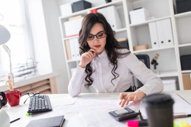 Genç bir kız ofis masa başında oturuyor ve hesap makinesinde nimet.