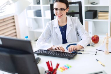 Beyaz bir elbise içinde güzel bir genç kız masada oturan ve klavyede yazarak.