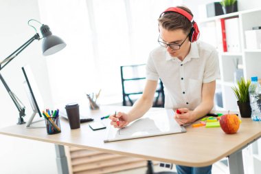 Gözlüklü ve kulaklıklı genç bir adam manyetik tahtaya bir işaret çizer..