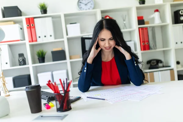 A beautiful young girl sits in the office at the table and holds her hands behind her head. — Stock Photo, Image