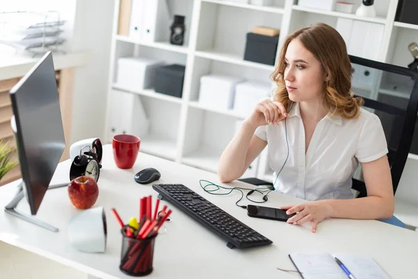 Gadis muda yang cantik bekerja dengan komputer di kantor. Gadis itu memiliki lubang suara dan telepon di depannya . — Stok Foto