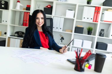 Güzel genç kız ofiste belgelerle masada çalışıyor ve bir kalem elinde tutuyor.