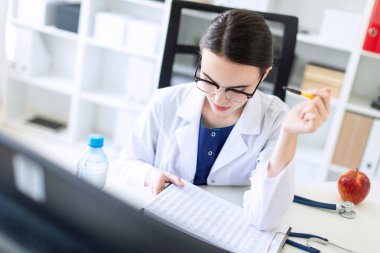 Beyaz bir elbise içinde güzel bir genç kız bir bilgisayar masası onun elinde belgeler ve bir kalem ile oturuyor. Alan, kız odak derinliği ile fotoğraf.