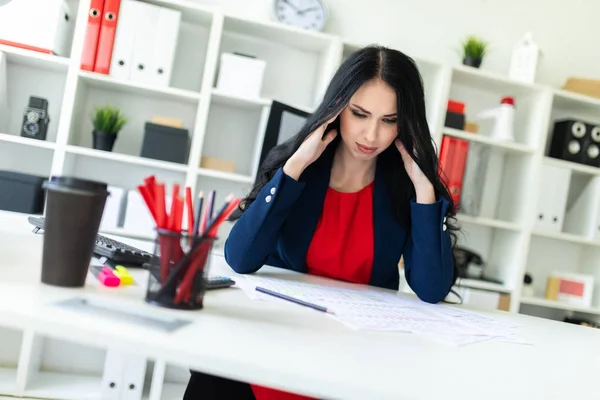 Ein schönes junges Mädchen sitzt im Büro am Tisch und hält die Hände hinter dem Kopf. — Stockfoto