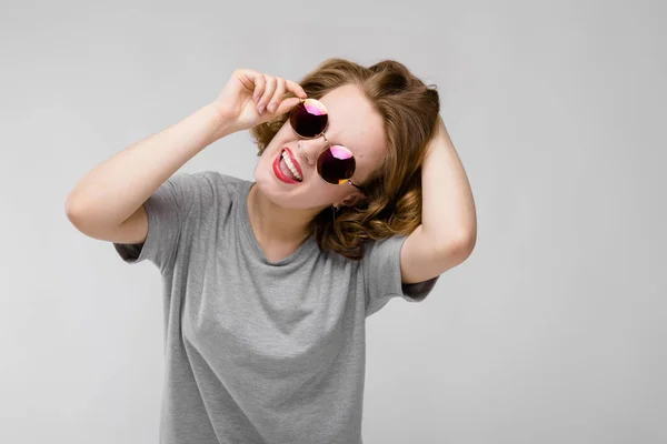 Menina encantadora em uma camiseta cinza em um fundo cinza. Menina alegre em óculos redondos — Fotografia de Stock