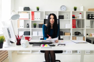 Genç bir kız masada ofiste oturur, onun elinde bir kalem tutan ve belgeleri doldurur.