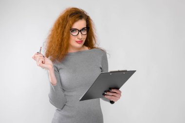 Kızıl saçlı Sevimli Genç kız. Bir gri Kazak bir genç kız. Gri bir arka plan üzerine genç kız. Gözlüklü genç bir kız eline bir kalem ve defter tutan