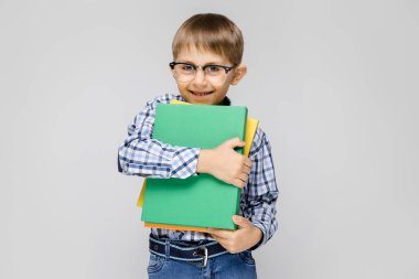 Bir vkletchatoy gömlek ve ışık kot büyüleyici bir çocuk gri bir arka plan üzerinde duruyor. Çocuk elinde belgeler ile çok renkli bir klasör tutar.