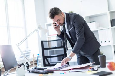 Bir adam ofiste bir tabloda yakın duran, telefonda konuşurken ve belgeler üzerinden çevirme.