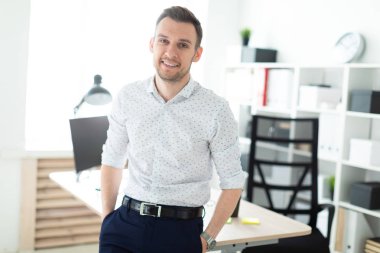 Genç bir adam ofiste bir masaya yaslanmış duruyor..