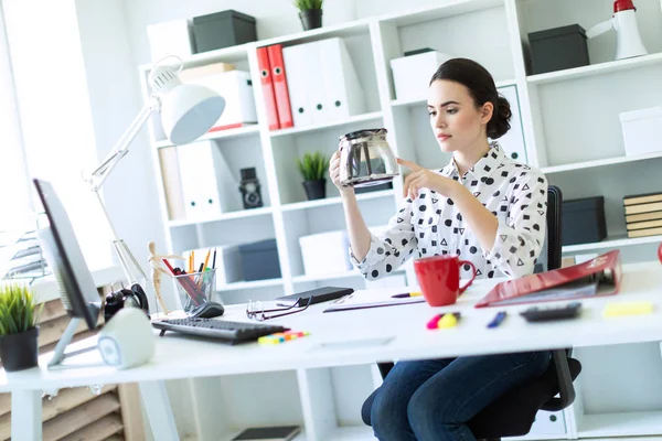 Een jong meisje zit aan een tafel in het kantoor en houdt een koffiepot. — Stockfoto