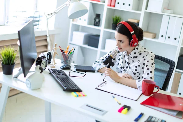 Güzel genç kız kulaklık bir mikrofon ofis masasında oturmuş. — Stok fotoğraf