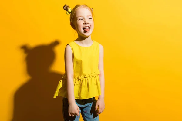 Girl with red hair on a yellow background. The girl shows her tongue. — Stock Photo, Image