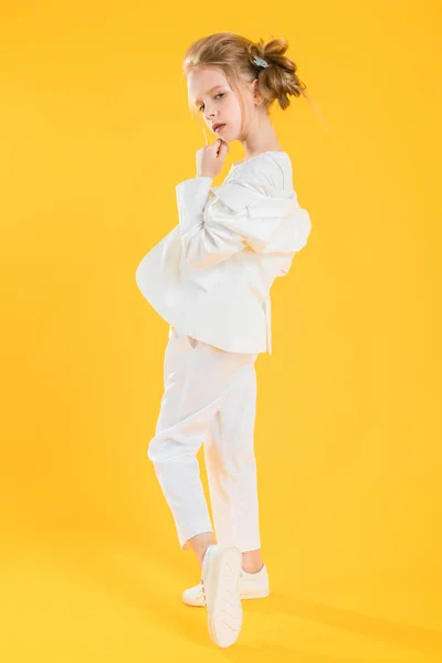 Dospívající dívka v bílých šatech pózující na žlutém pozadí. Dívka si položila bundu na lokty.. — Stock fotografie