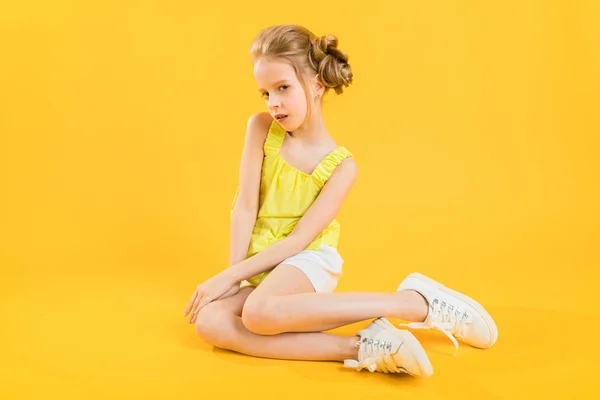 A teenage girl is sitting on a yellow background. — Stock Photo, Image