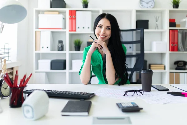 Mladá dívka sedí u stolu office a drží tužku v ruce. — Stock fotografie