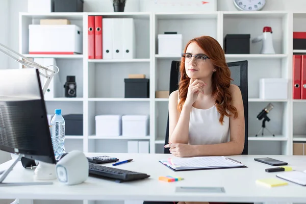 Beautiful young girl is sitting at the desk in the office.