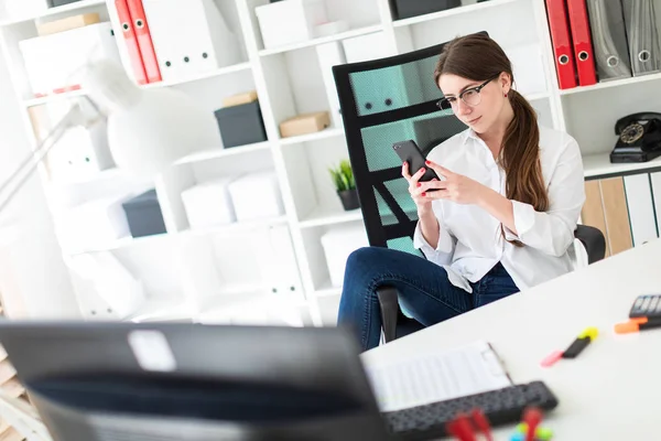 Genç bir kız ofiste bir masada oturur, onun ayak üzerinde kol dayama atar ve telefona benziyor.