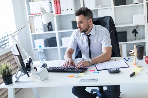 Bir adam belgeleri ve bir bilgisayar ile çalışma ofisinde, bir masada oturuyor.