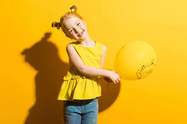 Ragazza con i capelli rossi su sfondo giallo. La ragazza sta tenendo un palloncino giallo con entrambe le mani . — Foto Stock