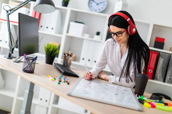 Genç bir kız kulaklık tablo anlamına gelir ve bir işaretleyici manyetik bir tahtaya çizer.