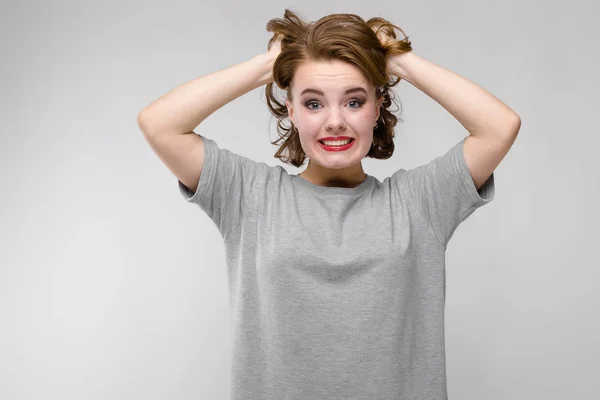 Charming young girl in a gray T-shirt on a gray background. The girl holds her hands behind her head and screams — Stock Photo, Image