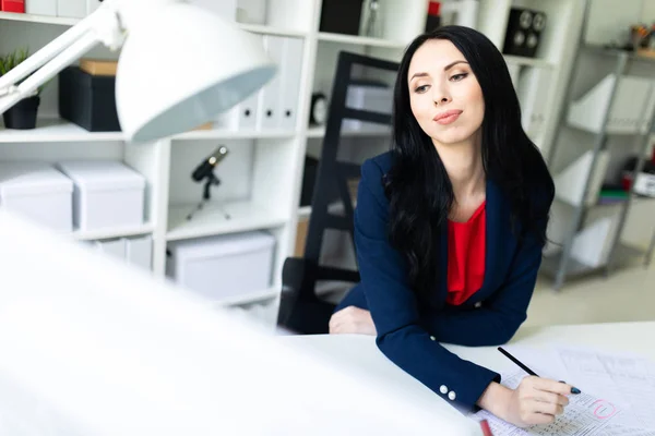 Hermosa joven está mirando a través de documentos, sentado en la oficina a la mesa . — Foto de Stock