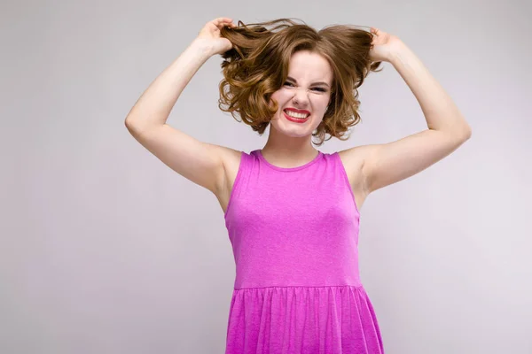 Charmante junge Mädchen in rosa Kleid auf grauem Hintergrund. ein junges Mädchen hält ihr Haar in den Händen — Stockfoto