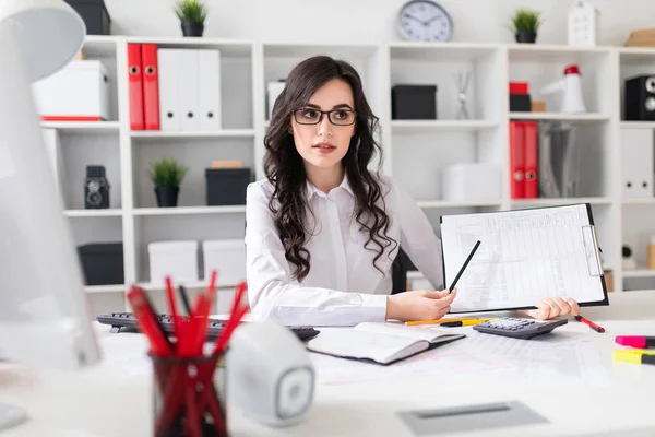 Een mooi jong meisje is zittend aan een tafel in het kantoor en een potlood wijzend op de informatie in het document. — Stockfoto