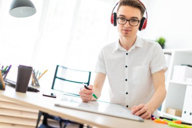 Gözlüklü ve kulaklıklı genç bir adam manyetik tahtaya bir işaret çizer..