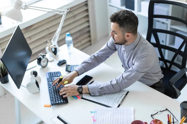 Un giovane in ufficio si siede a un tavolo, tiene in mano un pennarello e lavora con documenti e un computer . — Foto Stock