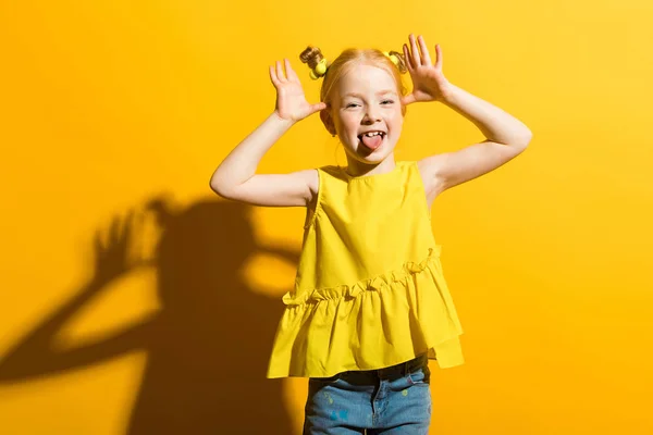 Dívka s červenými vlasy na žlutém podkladu. Dívka ukazuje její jazyk. — Stock fotografie