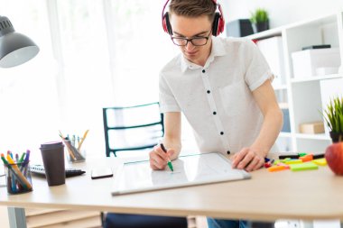 Gözlüklü ve kulaklıklı genç bir adam manyetik tahtaya bir işaret çizer..